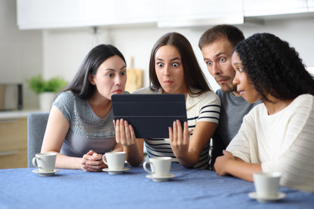 Perplexed group of friends checking tablet in the kitchen at homeの写真素材