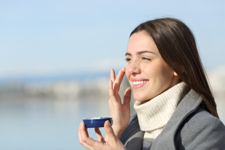Happy woman in winter applying hydration cream on cheekの写真素材