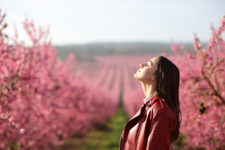 Profile of a woman in red jacket breathing fresh air in a flowered pink fieldの写真素材