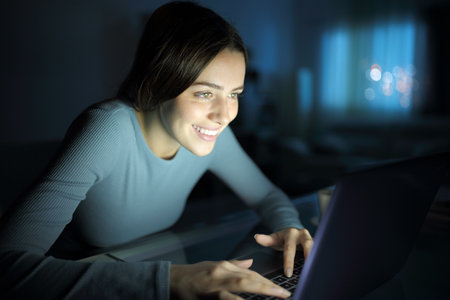 Happy woman using laptop typing in the night on a desk at homeの写真素材