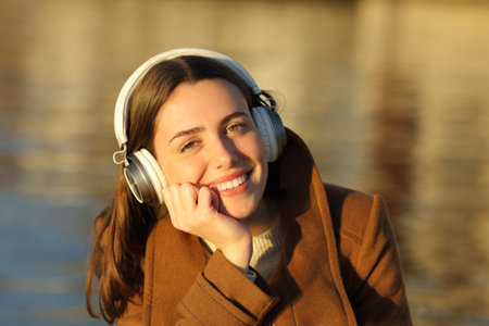 Happy woman in winter wearing headphone listening music looks at you at sunsetの写真素材