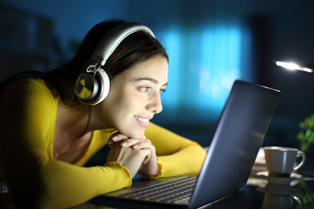 Happy woman with headphone in the night watching media on laptop at homeの写真素材