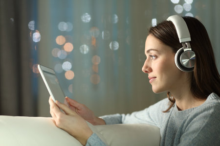Profile of a female wearing headphone watching media on tablet in the night at homeの写真素材