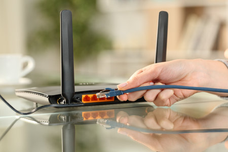 Close up of a hand plugging network cable to a modem on a desk at home