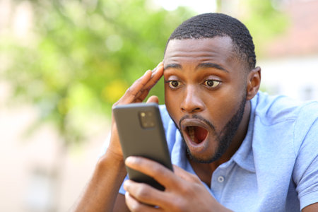 Amazed black man checking smart phone in a park