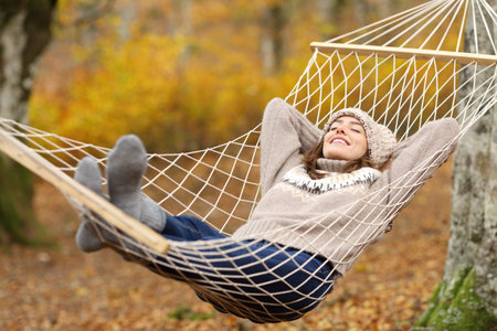 Full body portrait of a happy woman lying on hammock in autumn forestの写真素材