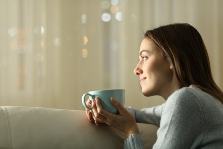 Relaxed woman thinking and drinking coffee in the night at homeの写真素材