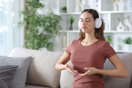 Woman wearing headphone doing guided breathing exercises sitting on a couch at homeの写真素材