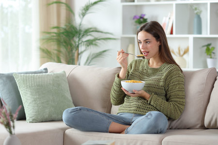 Woman in green eating cereals for breakfast sitting on a sofa at home