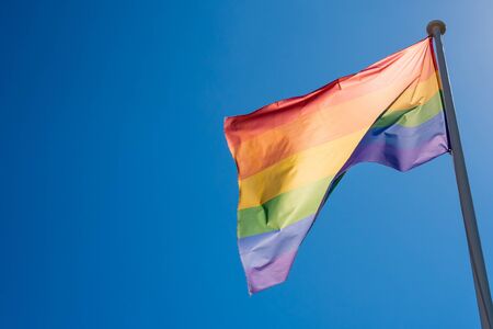 LGBT pride flag hung on a mast and waving in the blue skyの写真素材