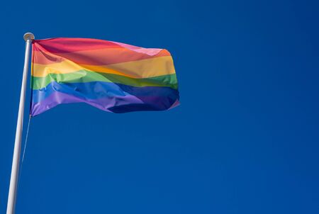 LGBT pride flag hung on a mast and waving in the blue sky