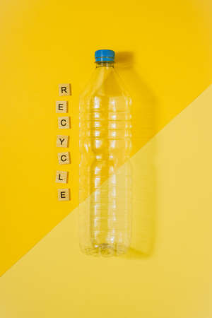 Vertical color image with an overhead view of a clear plastic bottle with blue cap on a yellow background and the word recycle. Recycling and environment concept.の写真素材