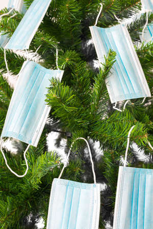 Vertical color image with a front view of a Christmas tree decorated with coronavirus masks. Covid...