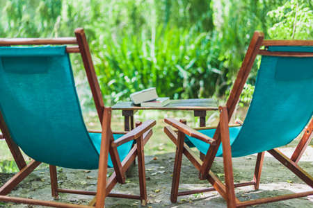 Horizontal color image with a side view of a wooden beach chairs in the garden and some books on the garden. Relaxing place concept.の写真素材