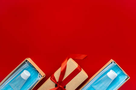 Horizontal color image with an overhead view of a packing a Christmas present during Coronavirus epidemic. Face masks and hydroalcoholic gels inside a cardboard box decorated with a bow on a red background.の写真素材