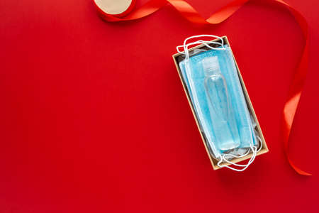 Face masks and hydroalcoholic gel inside a cardboard box decorated with a bow on red