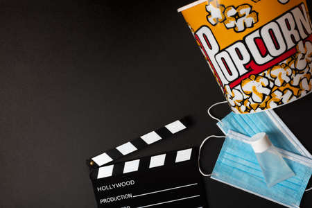 Horizontal color image with an overhead view of a movie clapperboard, hydrogel, face mask, and popcorn box on a black background during the second wave of the coronavirus pandemic. Covid concept.の写真素材