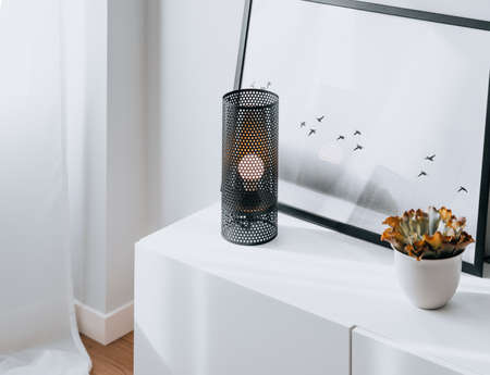 black deployÃ© lamp with lit bulb resting on top of a white wooden cabinet with a minimalist...