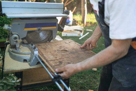 detail of adult male arms holding a board to be cut and a pencil to mark the location of the cut on...