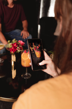 girl sharing on media a photo of an orange cocktail at night in a club through her smart phone