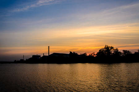 Factory located near the river on sunset background.