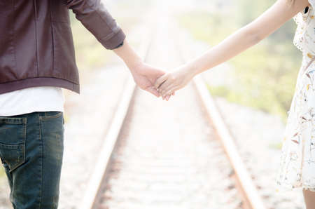 Young loving couple walking hand in hand on railway tracks looking with sunrise background.の写真素材