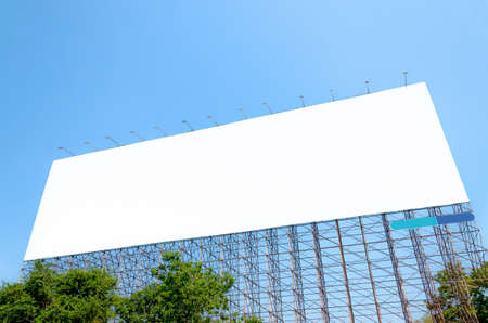 Large blank billboard located on the side of the road with blue sky background.