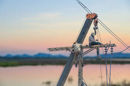Technician men fixing or repairing power line on electric pole on sunset backgroundのeditorial素材