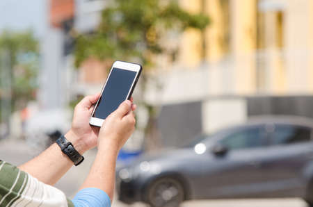 Hands are holding touch screen smart phone on blurred building and car background.の写真素材