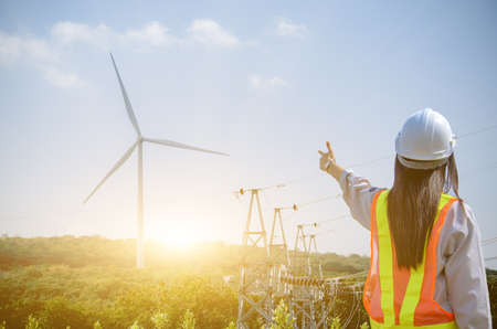 female engineer stands at a wind turbine power station against the backdrop of the sunrise.