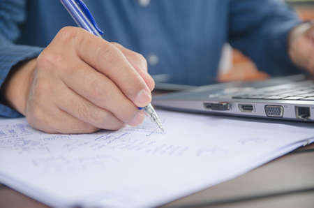 man holding a pen in his hand with a laptop on the table