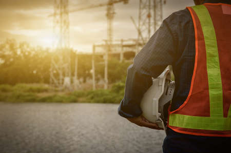 white helmet in the hands of an engineer with a sunset on the building construction backgroundの写真素材