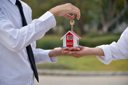 Hand holding keys and hand holding model house on blurred nature background, real estate concept
