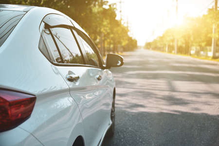 white car parked along the road against a natural backdrop with bright sunlight, focal point on the passenger door handle.の写真素材