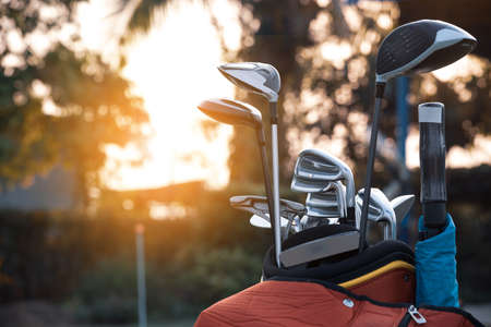 Golf bag and golf clubs placed on golf course against sunset backgroundの写真素材