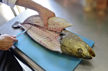 Details filleting fish on a cutting board in a restaurant kitchenの写真素材