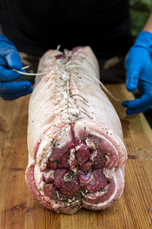 Butcher binds meat rolled up for pochette roast pork on cutting boardの写真素材
