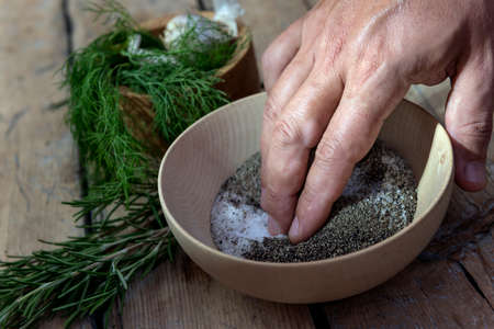 Hand in a wooden bowl mixes salt and pepper and aromatic herbs