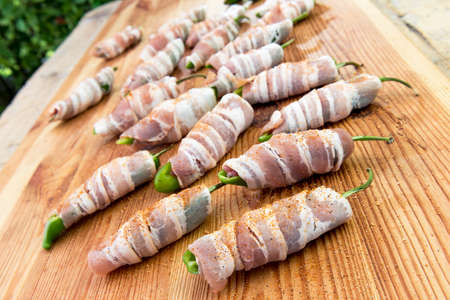 Peppers stuffed with cheese and minced meat and covered with bacon on cutting board ready for cookingの写真素材