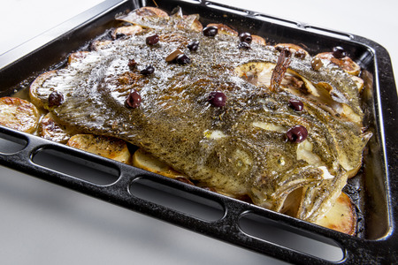 Cooked Whole Turbot fish in baking pan oven with potatoes olives and aromatic herbs isolated on...