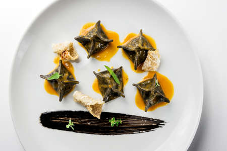 Top view of Plate with black ravioli stuffed with cod and shellfish bisque