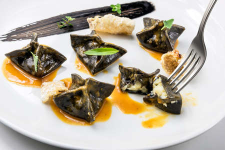 Plate of black ravioli stuffed with cod with shellfish bisque and forkの写真素材