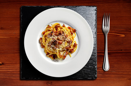 Top view of white Plate with spaghetti carbonara with grated cheese and fork on black stoneの写真素材