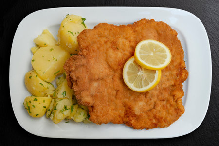 Top view of Schnitzel Classisc Viennese Veal Cutlet with potato salad and lemon slices on black stoneの写真素材