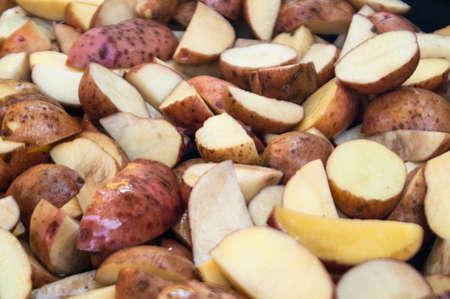 potatoes cut by pieces in a peel before frying on a plateの写真素材