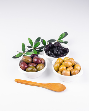 Olives in bowls isolated on white, olive branch in the background.