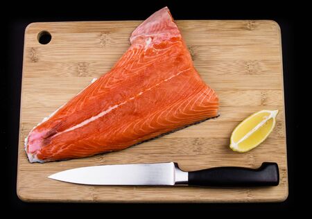 Salmon on a chopping board, knife and lemon.