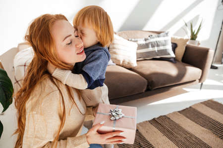 Little cute red haired boy gives mom a new year giftの写真素材