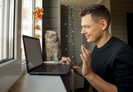 Happy young man with cat at home using video to congratulate Merry Christmas his relatives.の写真素材