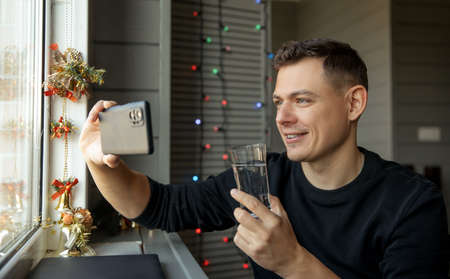 Young man with glass making video calling to congratulate Merry Christmas his relatives.の写真素材